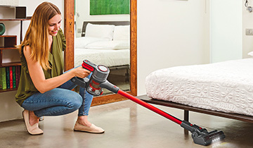 The image shows a girls who vacuums under the bed with Polti Forzaspira D-Power SR510