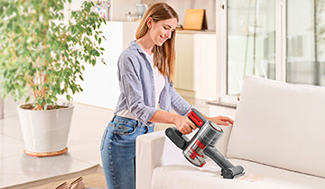 The image shows a girs who vacuums the sofa with the portable Polti Forzaspira D-Power SR550