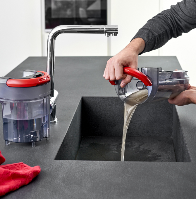 una persona che versa il contenuto di una tanica di acqua sporca in un lavabo